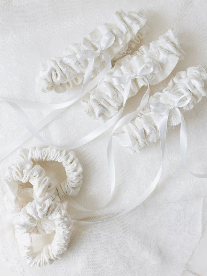 wedding garter heirlooms with white lace from mom's wedding dress and white satin details and bow alongside scrunchies made from mother of the bride's dress materials handmade by The Garter Girl