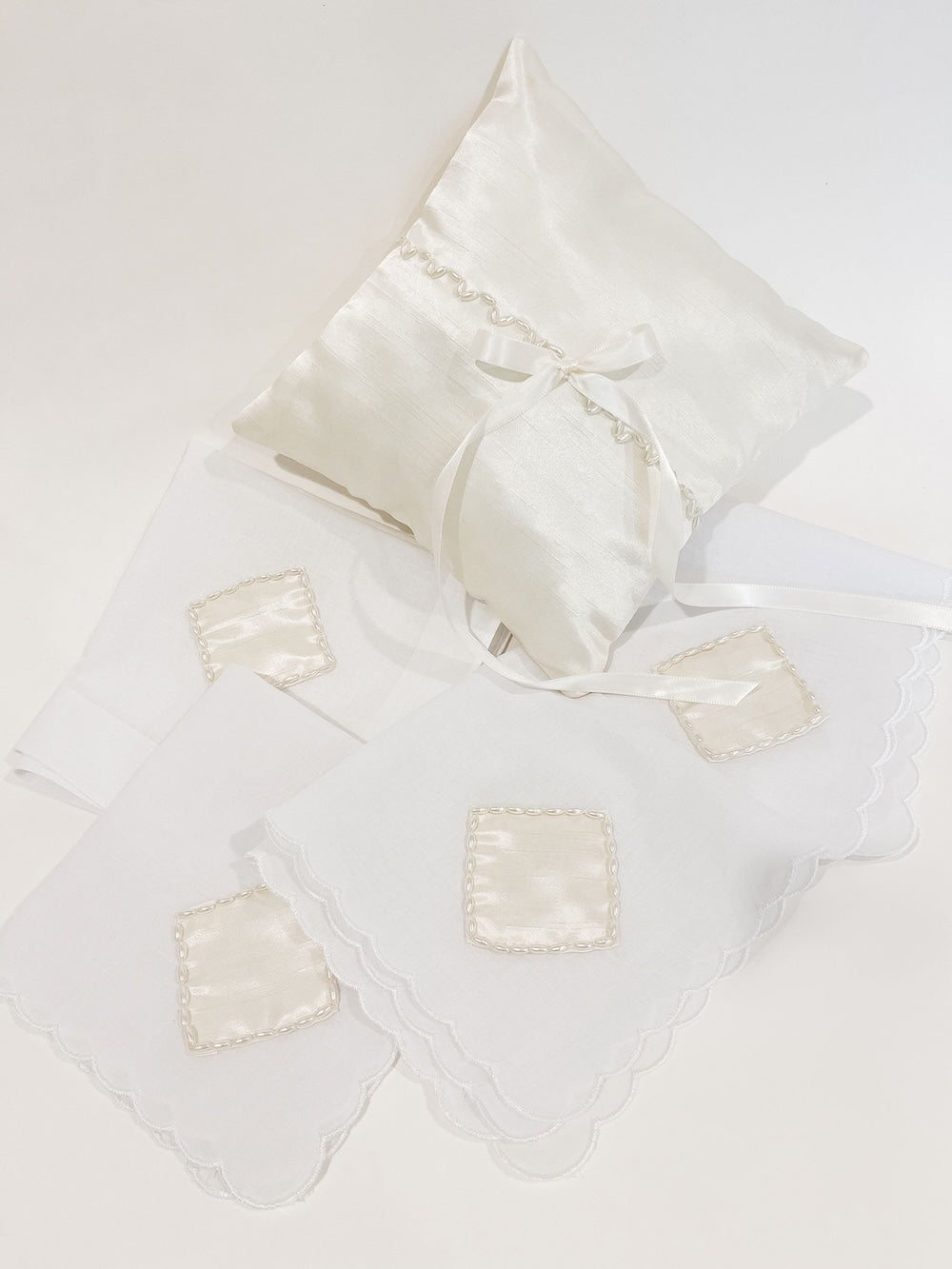 ivory satin ring bearer pillow with pearl detailing and a long ivory satin bow alongside four cotton handkerchiefs with heirloom patches and pearls handmade by The Garter Girl