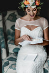 lace wedding garter being opened by bride in lace wedding dress with colorful flower crown by The Garter Girl