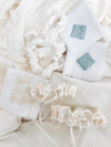 hand embroidered handkerchiefs with blue satin patches and ivory lace along with ivory scrunchies with short ivory satin bows with ivory lace and satin wedding garters and ivory satin long bows handmade by The Garter Girl